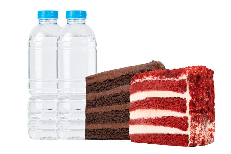 A slice of red velvet cake next to a slice of chocolate fudge cake with two bottles of water.